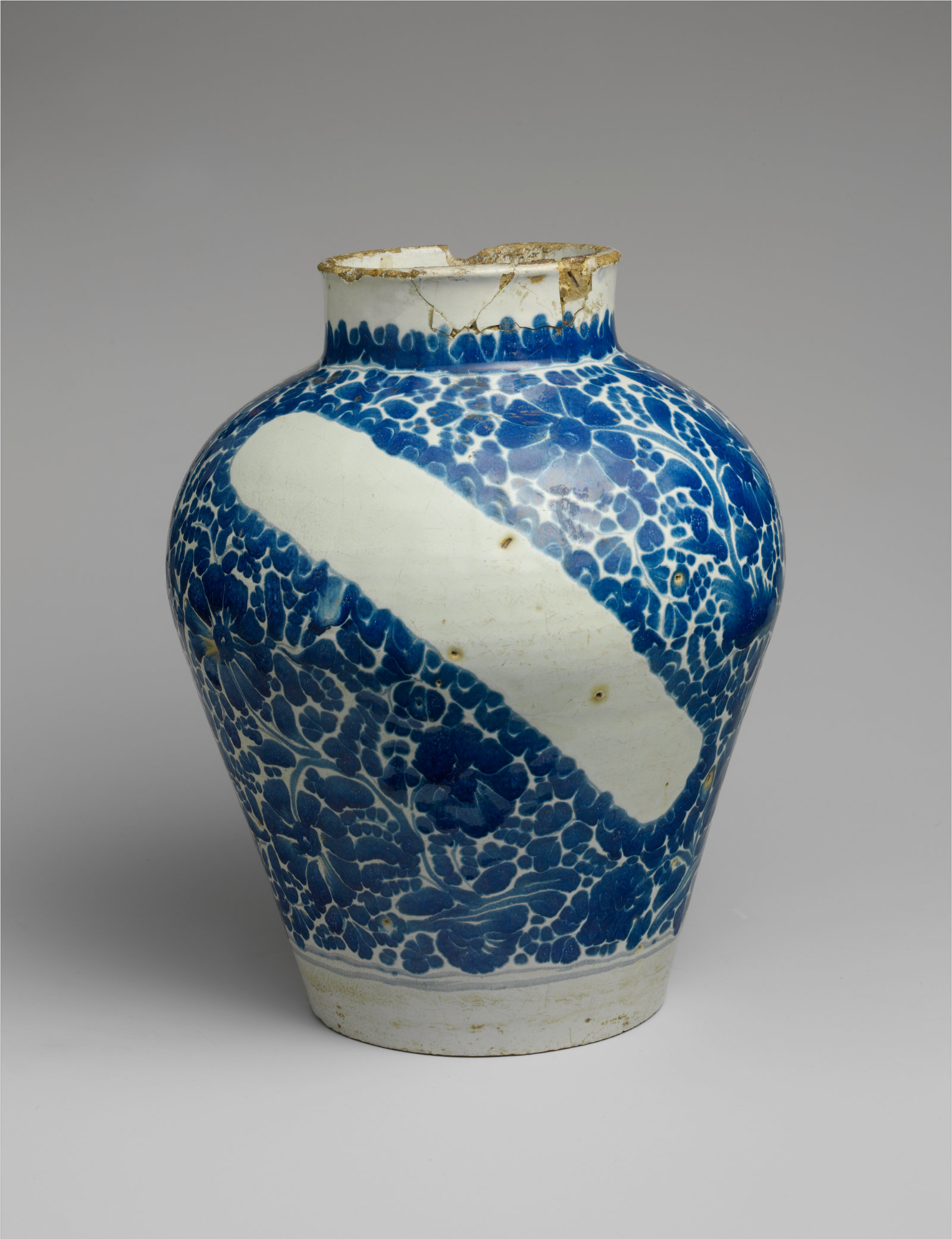 A white bulbous vessel heavily decorated with blue floral motifs except for a void in the shape of a rectangle.