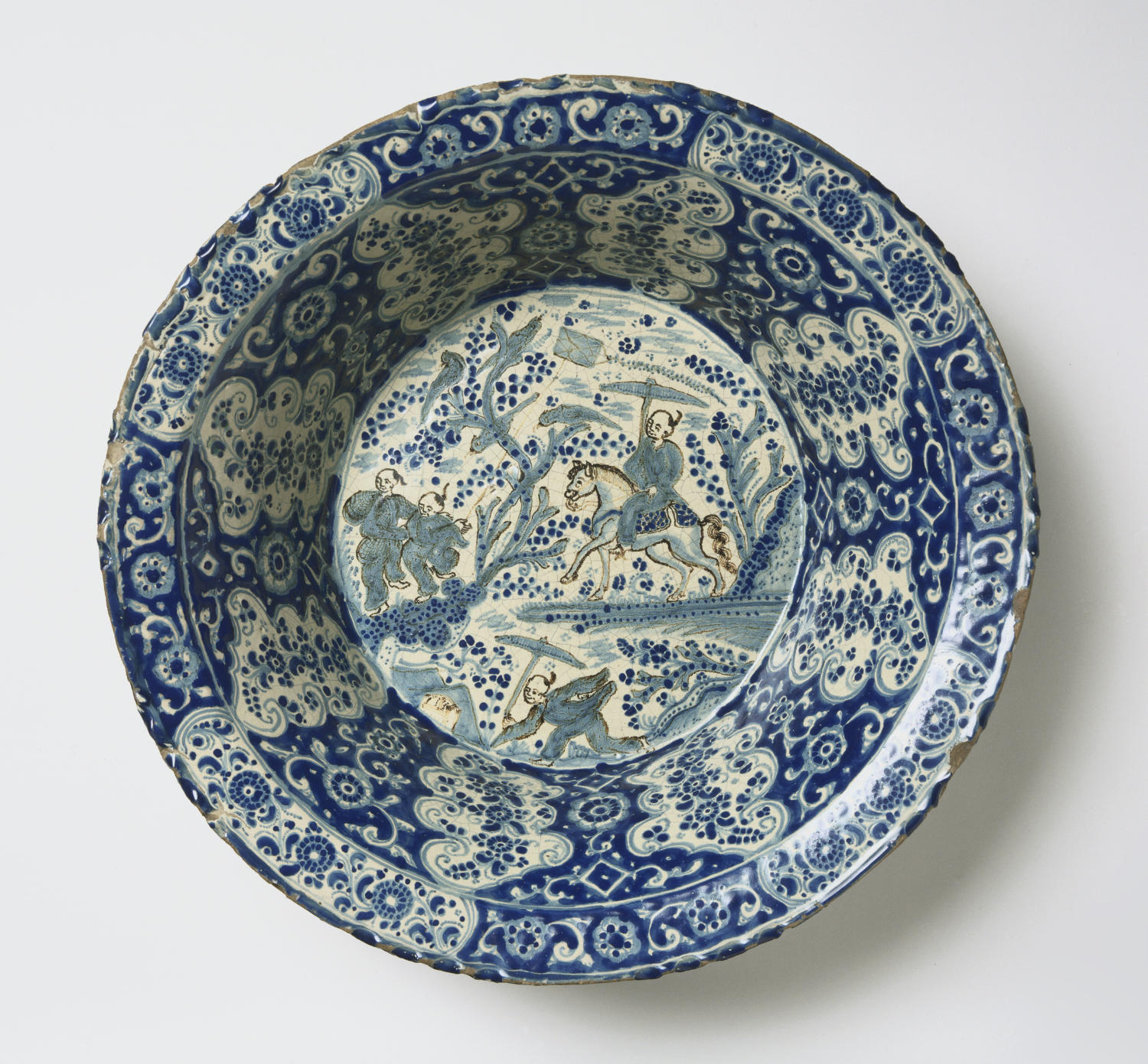 A blue and cream vessel features four men at center each sporting a mostly bald hairstyle with a single braid at the back of the head. One man rides a horse and carries an umbrella.