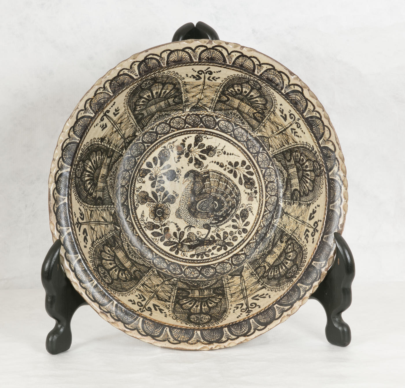 A cream plate or bowl decorated with curving black lines, with a strutting bird and floral motifs at center.