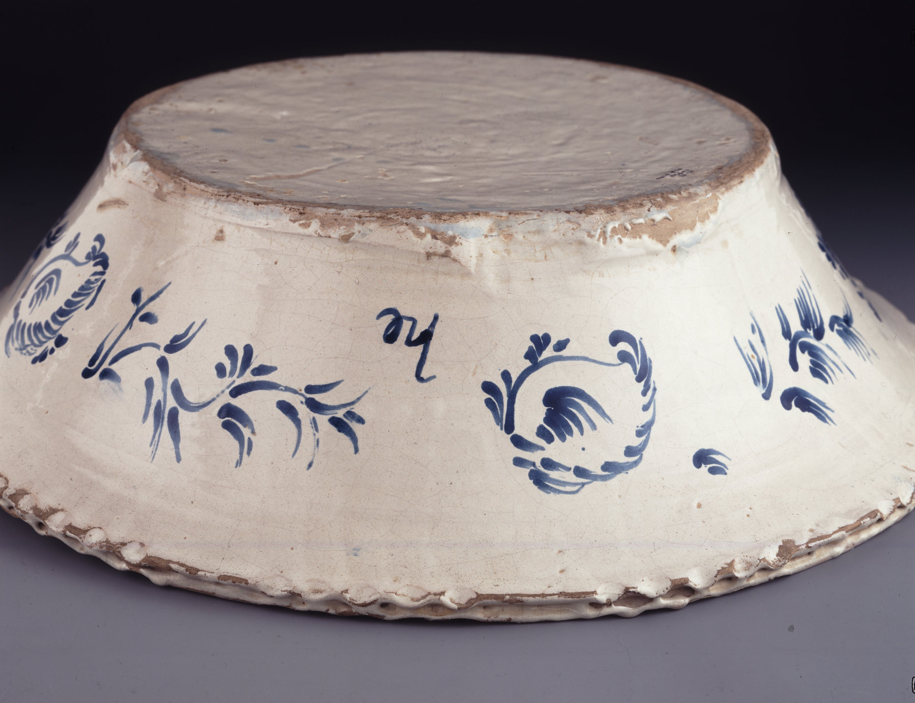 An overturned cream vessel decorated with blue vegetation motifs and featuring a mark that resembles he.