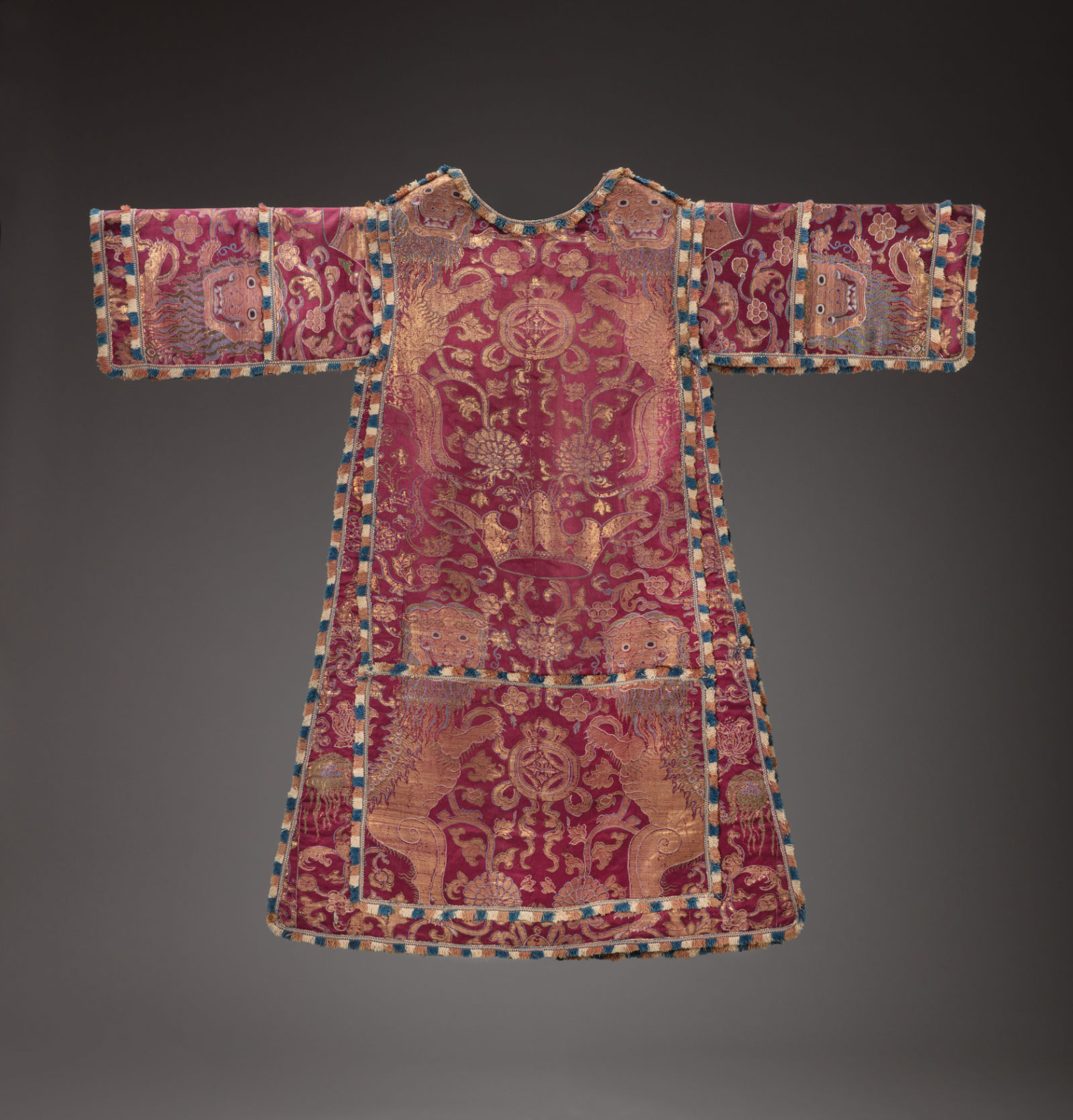 A red tunic with gold decorations featuring a crown at center, two animals (maybe lions) at bottom, floral motifs, and lion heads on each sleeve.