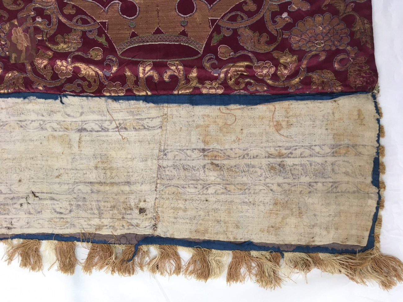 A close-up view of the white edge of a red and gold textile.