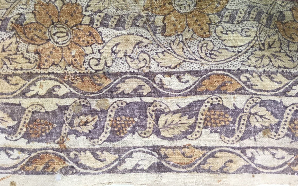 A close-up view of the white edge of a red and gold textile.