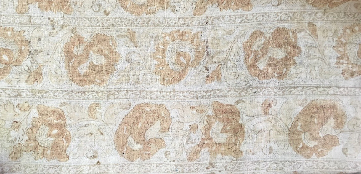 A close-up view of the underside of a red textile. The underside is cream colored with light red floral motifs.