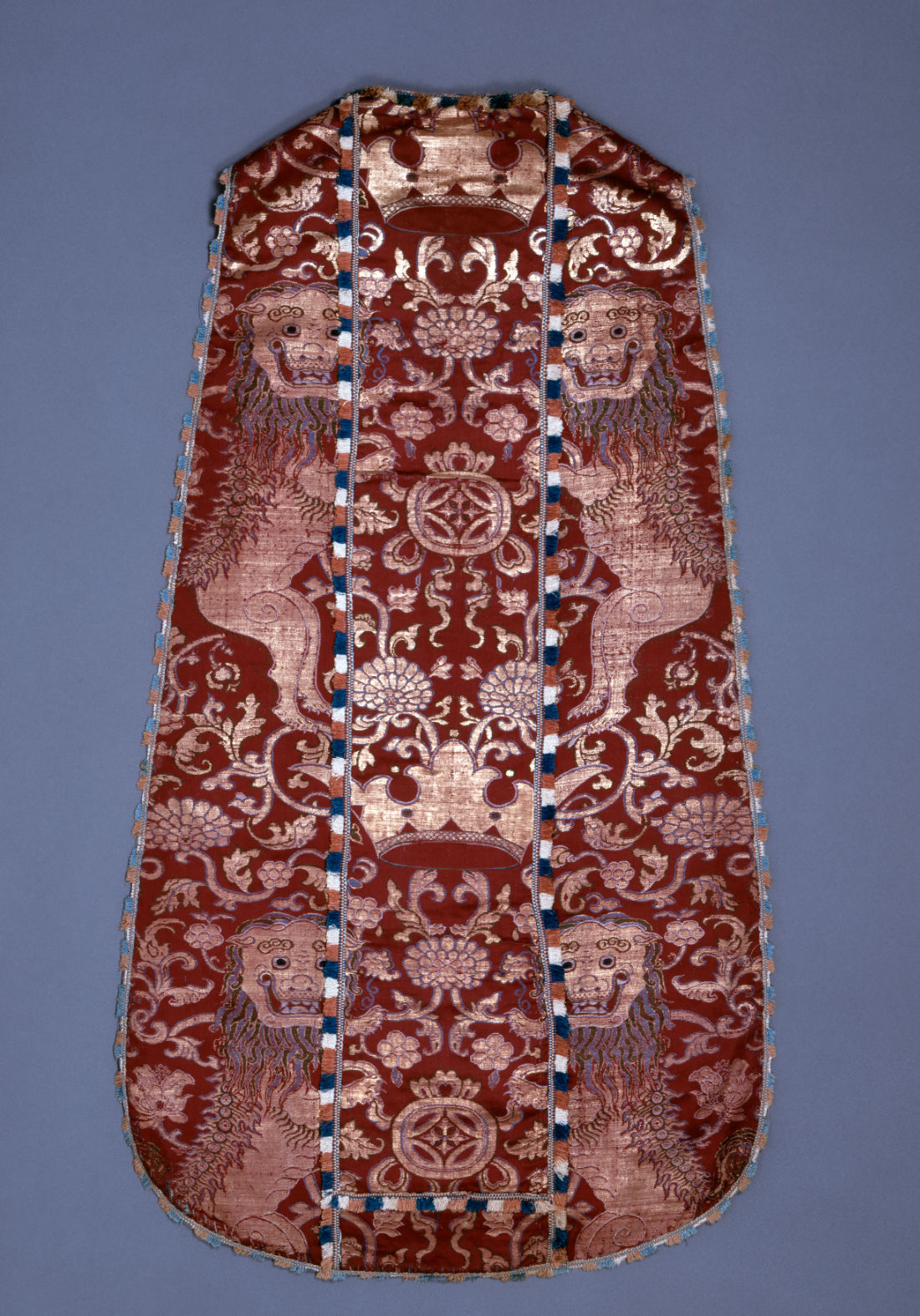 A long sleeveless red cloth with gold decorations featuring a crown at center and animals (likely lions) at left and right, and floral motifs throughout.