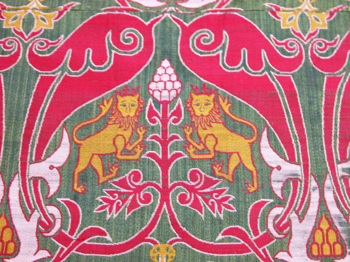 A close-up view of a green textile with two yellow lions and bright pink floral motifs.