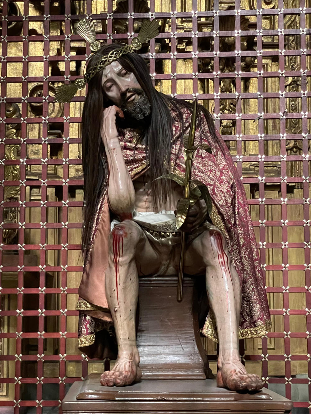 A sculpture of Christ leaning on one knee and wearing a red and gold mantle.