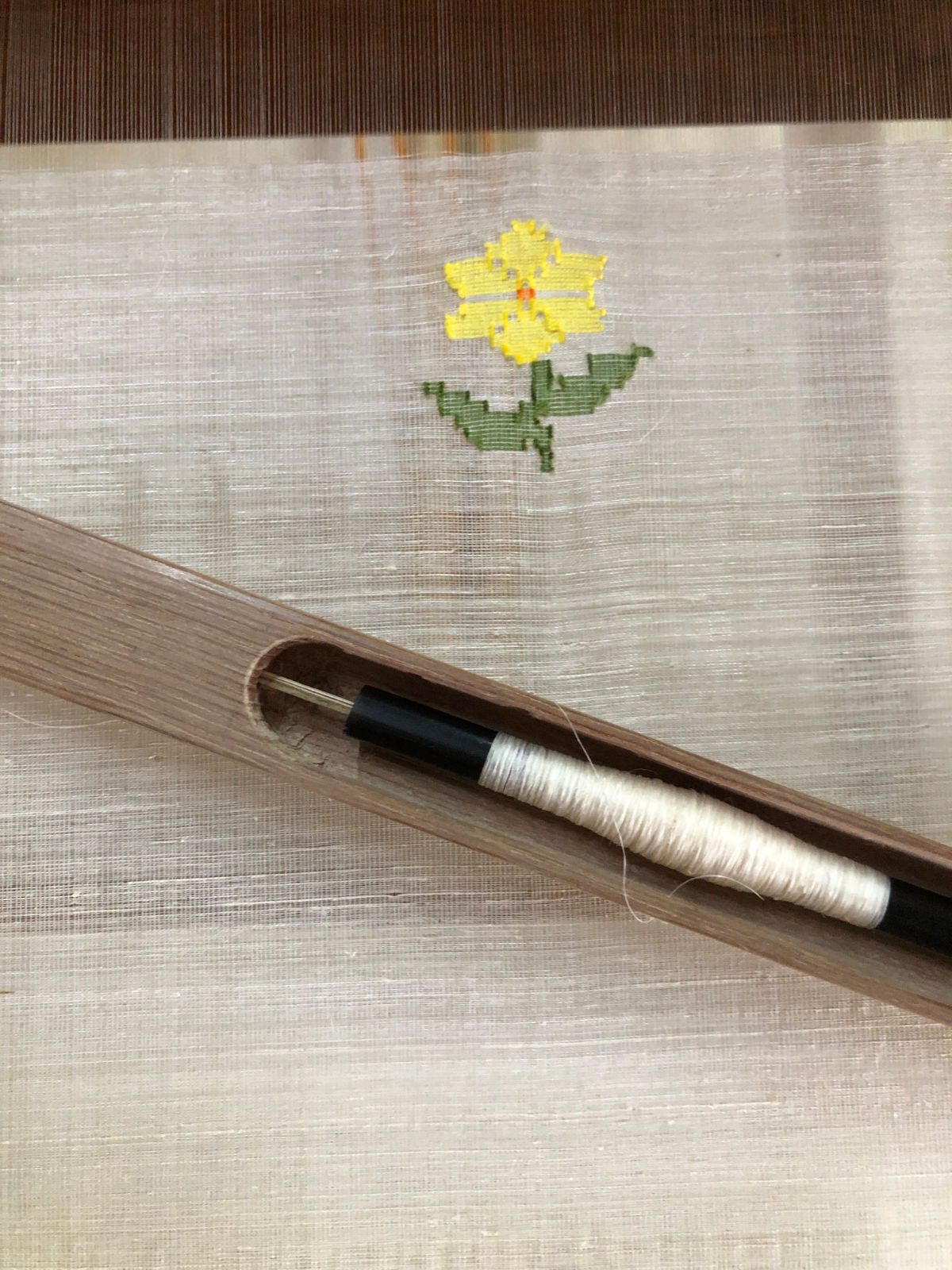 A photo of a wooden shuttle and bobbin resting on a piece of fabric.