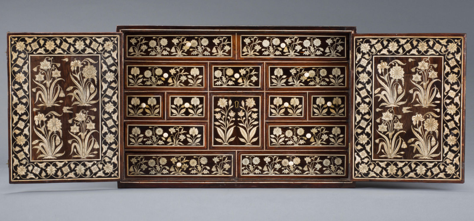 An open wooden cabinet with ivory floral motifs.