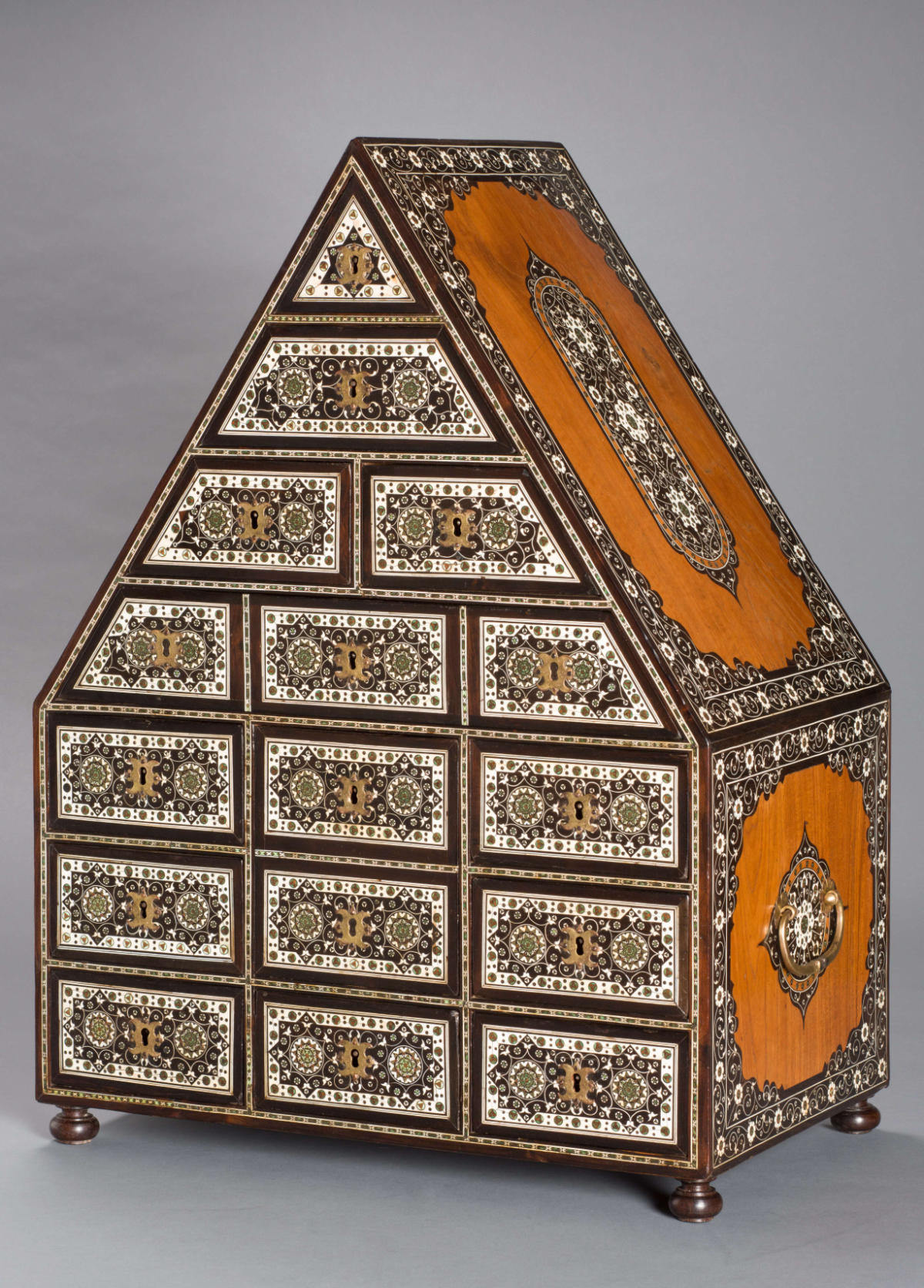 A triangular-shaped cabinet heavily ornamented in wood and metal.