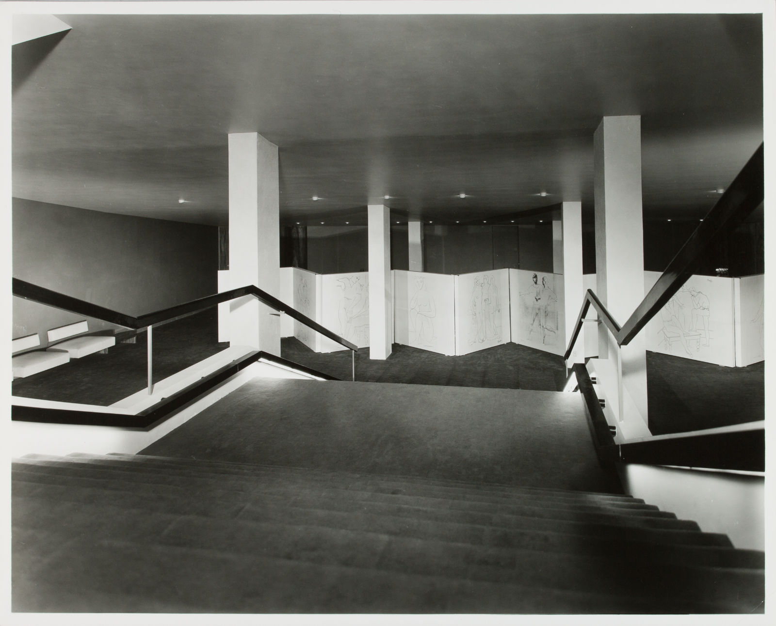 A black and white photo of a staircase leading to a large room with an oversized white biombo.