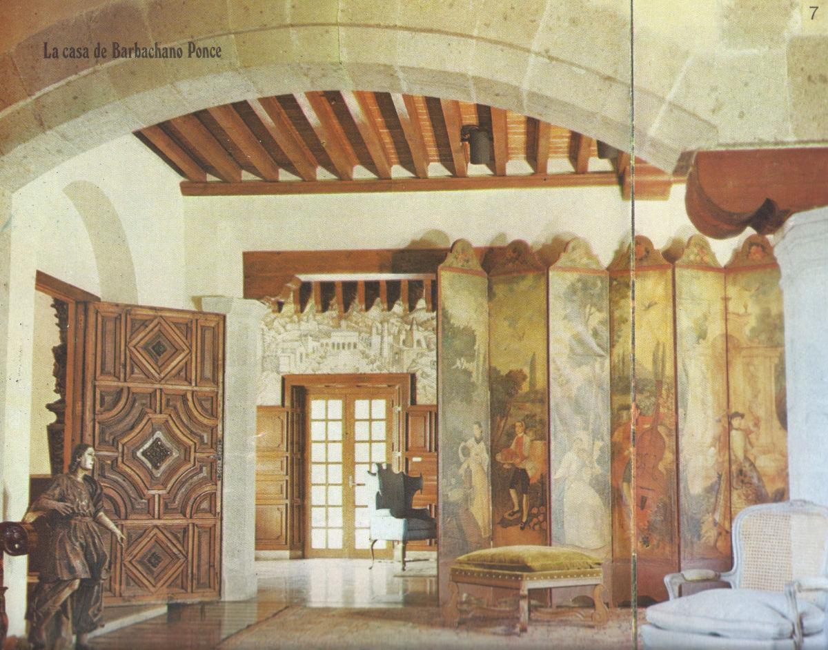 A scanned image of a home interior. A 6 panel biombo is pushed up against the wall on the right. The biombo depicts aristocratic men and women enjoying live music and food in the outdoors.