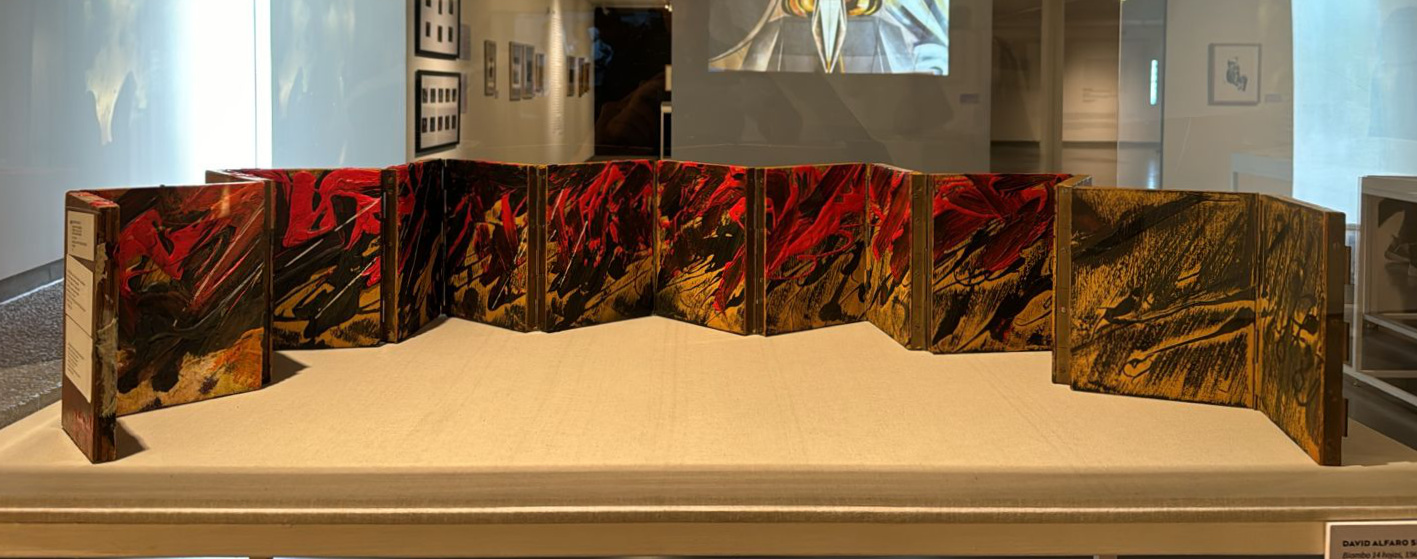 A long biombo with short square panels displayed in a gallery case. The panels are illustrated with gestural strokes of red and black paint.