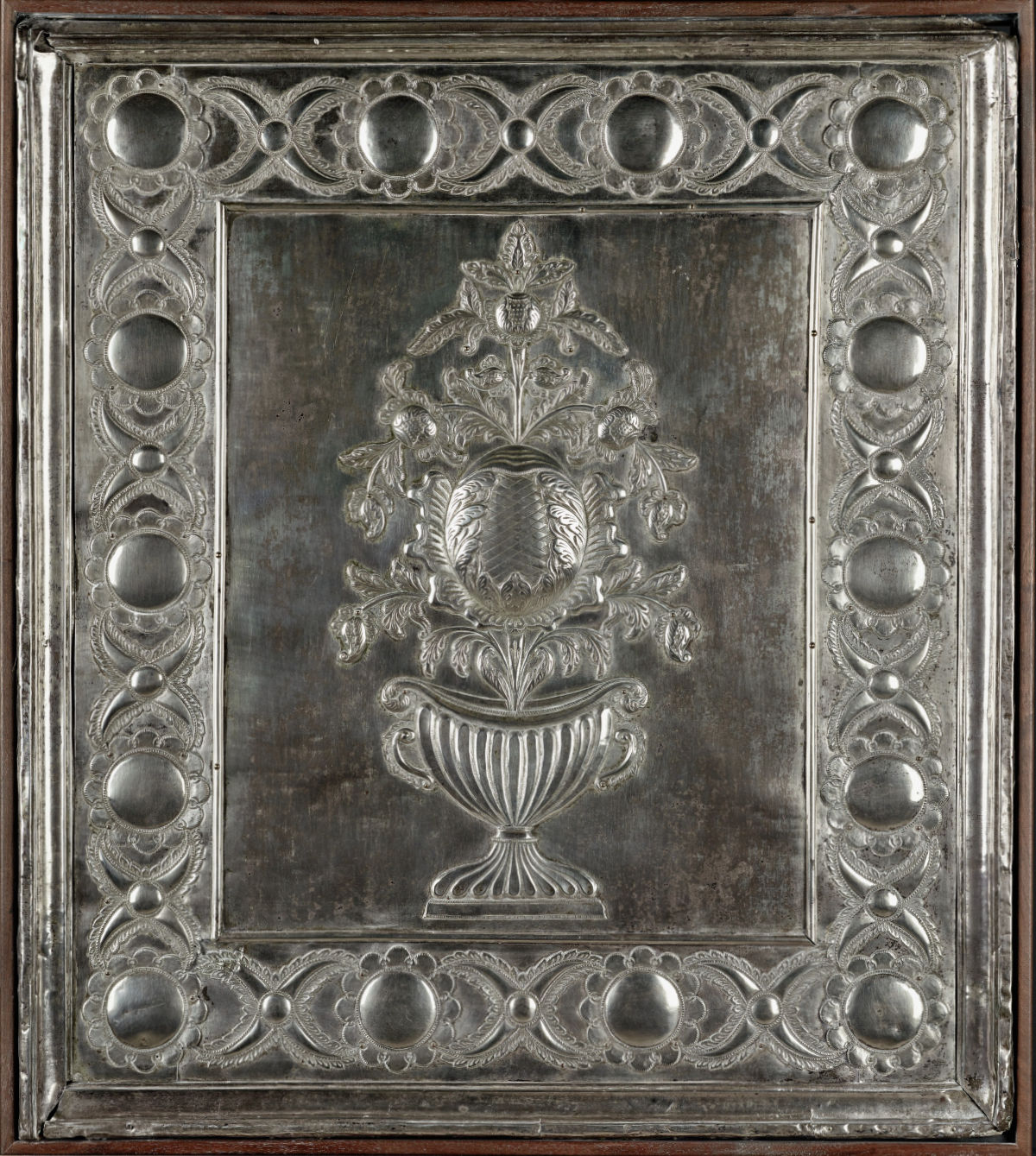 A rectangular silver panel with raised ornamentation.